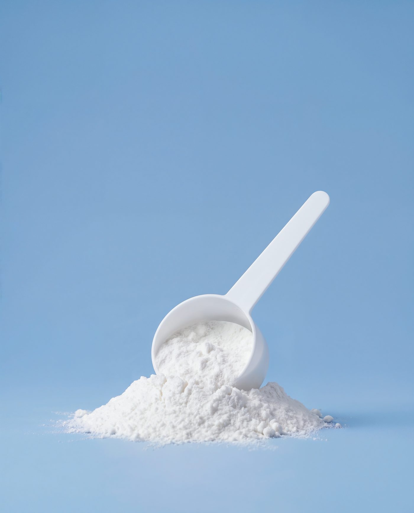 A measuring scoop of micronised creatine monohydrate powder on a blue background